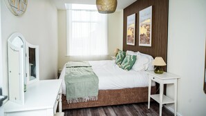 A bedroom with a bed, bedside tables, a hanging light fixture, a mirror, and a window.