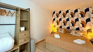 Ein Schlafzimmer mit einem Bett, einem Holzschrank, einem Nachttisch und einer Wand mit geometrischem Muster.