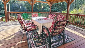 Una terraza techada al aire libre con techo de madera, una mesa con cojines estampados y un tapete con diseño.