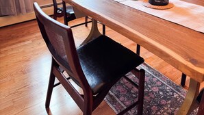 Un comedor con mesa de madera, sillas, un jarrón con flores secas y una vela.