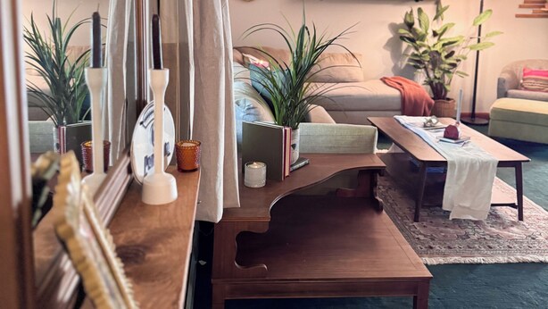 Una sala acogedora con una mesa de centro de madera, un sofá y una mesa de comedor. Hay plantas en macetas y un espejo en la pared.