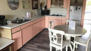 A compact kitchen with a sink, microwave, and refrigerator, a dining table with chairs, and a clock on the wall. - Unit 222 Beautiful Cedar key (Cedar Key)