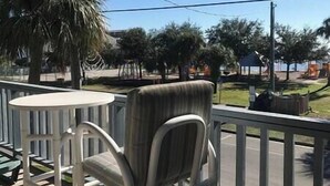 A balcony with a chair and a table, overlooking a street with trees and a building. - Unit 222 Beautiful Cedar key (Cedar Key)