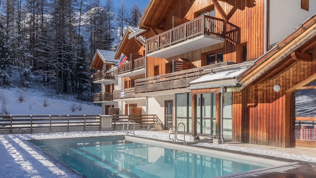 A wooden chalet with a pool, surrounded by snow-covered trees.