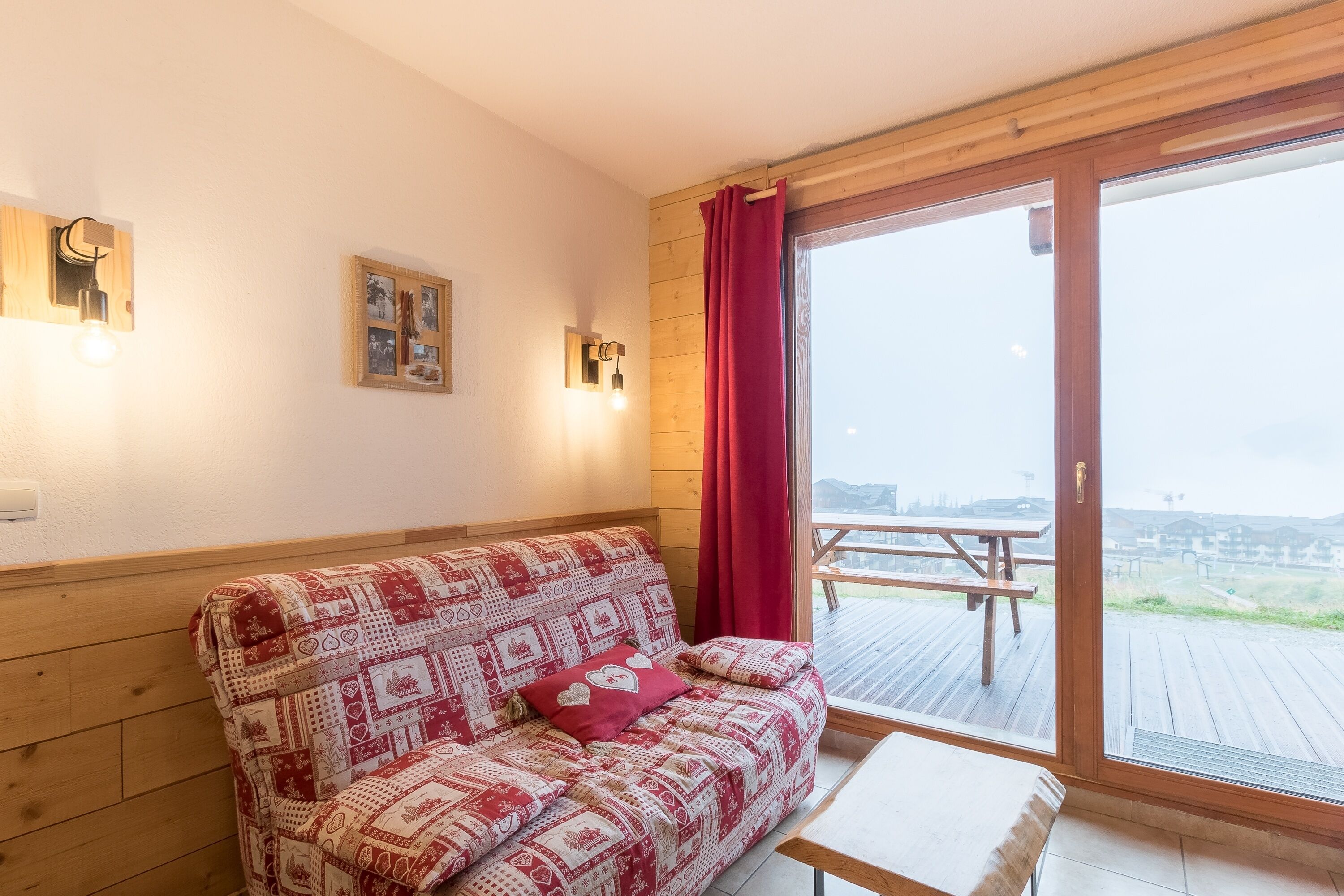 A cozy room with a wooden sofa, a small table, and a large sliding glass door leading to an outdoor deck.