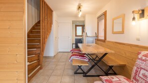 A wooden interior with a staircase, a dining table with benches, and a kitchen area in the background.