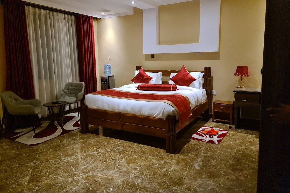 A hotel room with a large bed, a desk, a chair, a water dispenser, and a lamp.