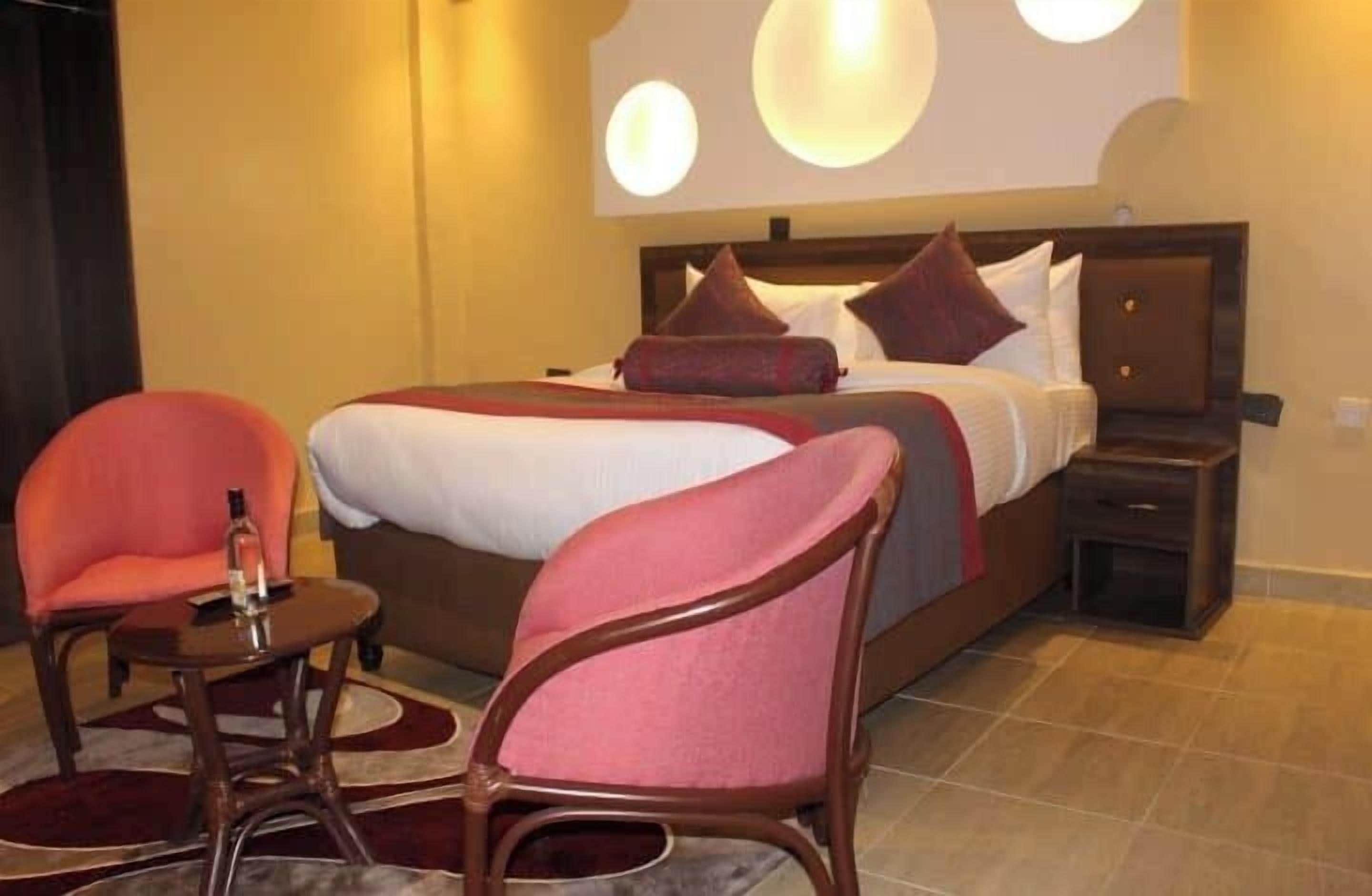 Ein Hotelzimmer mit einem großen Bett, zwei Sesseln, einem kleinen Tisch und einem Nachttisch.