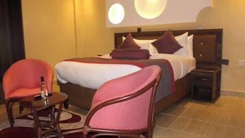 Ein Hotelzimmer mit einem großen Bett, zwei Sesseln, einem kleinen Tisch und einem Nachttisch.