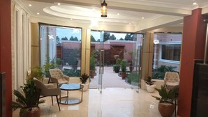 A spacious indoor area with a glass door leading to a courtyard, furnished with chairs and tables, and surrounded by potted plants. - Famous Gates Hotel Bomet  (Bomet)