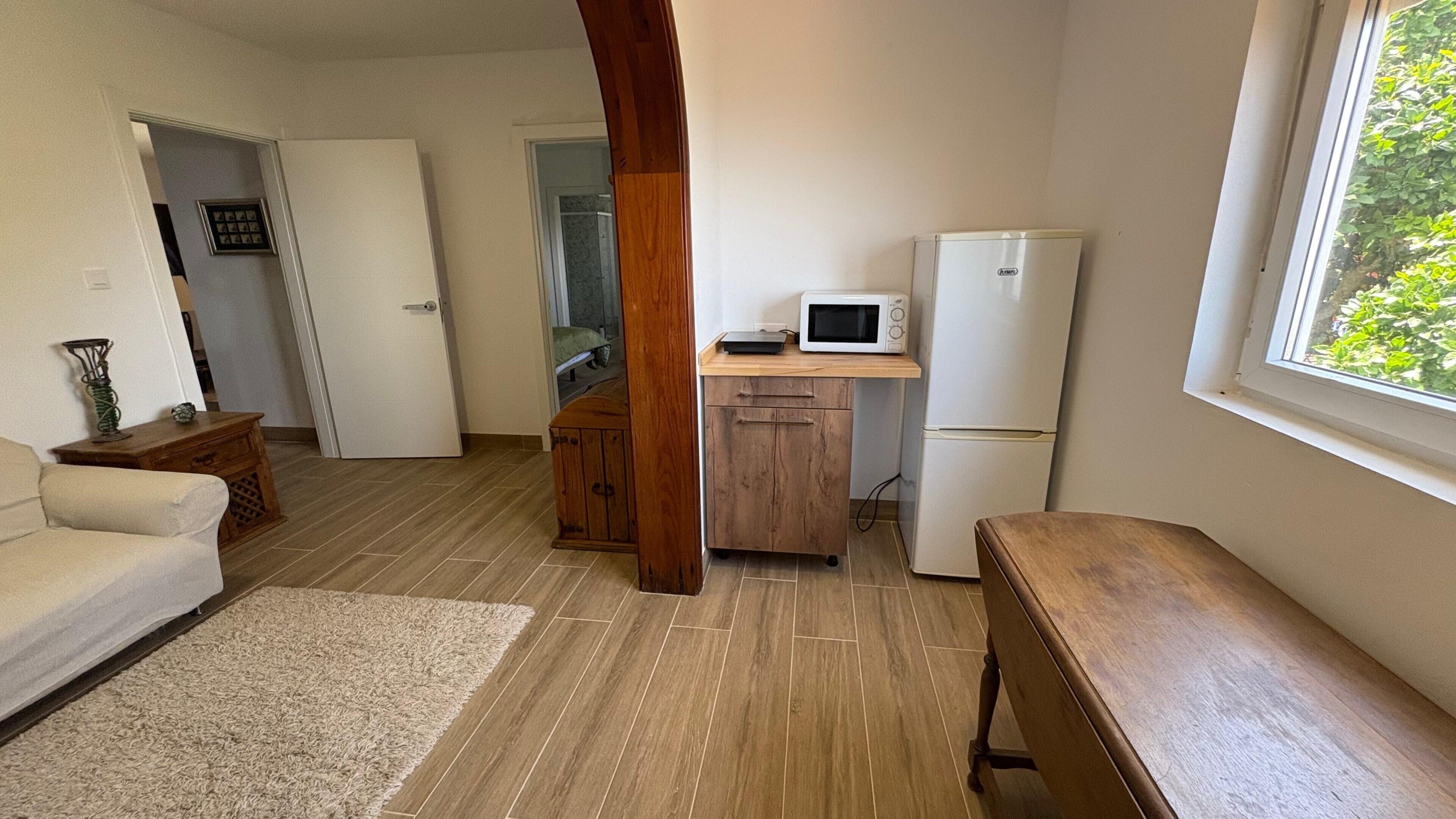 A compact living space with a kitchenette, a wooden bench, a white sofa, and a window with a view.