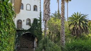 Un patio con un puente de piedra, abundante vegetación y un edificio blanco con ventanas arqueadas.