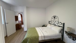 Ein Schlafzimmer mit einem Bett, einem Nachttisch, einer Lampe, einem Holzkasten und einer Tür zu einem anderen Raum.