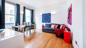 A modern living room with a dining area, a grey sofa, and a red side table.