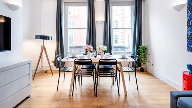 A modern dining area with a round table, black chairs, and a vase of flowers.