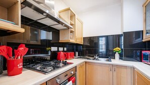 A modern kitchen with wooden cabinets, a gas stove, a sink, and a red utensil holder.