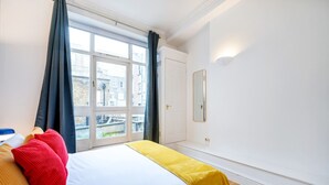 A hotel room with a bed, a window with curtains, a mirror, and a view of buildings outside.