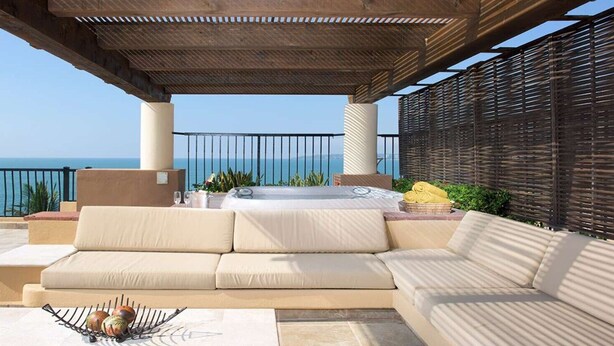 Un espacio de estar al aire libre techado con sofá, jacuzzi y vista al mar.