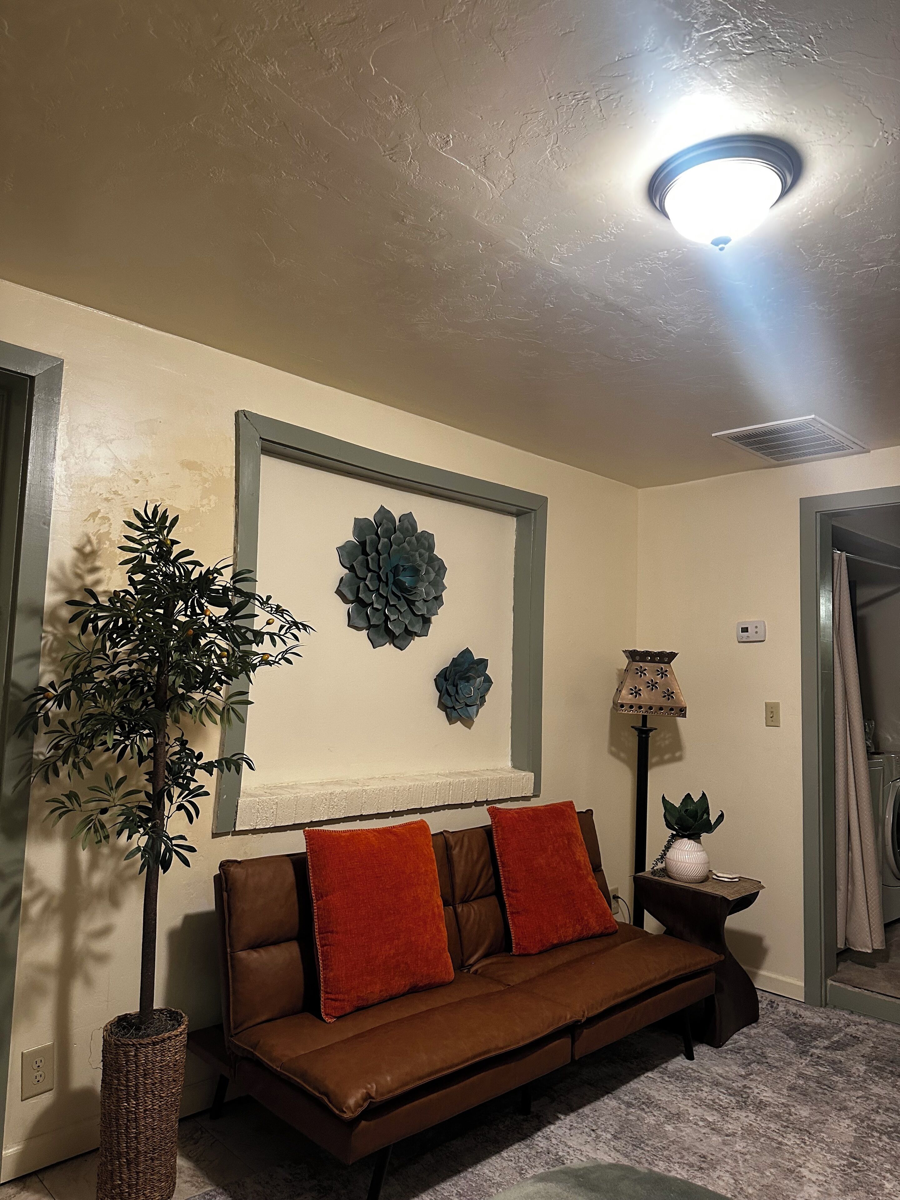 A living room with a brown leather sofa, a decorative wall piece, a potted plant, and a floor lamp.