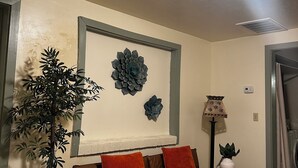 Een woonkamer met een bruine leren bank, een decoratief wandobject, een potplant en een vloerlamp.