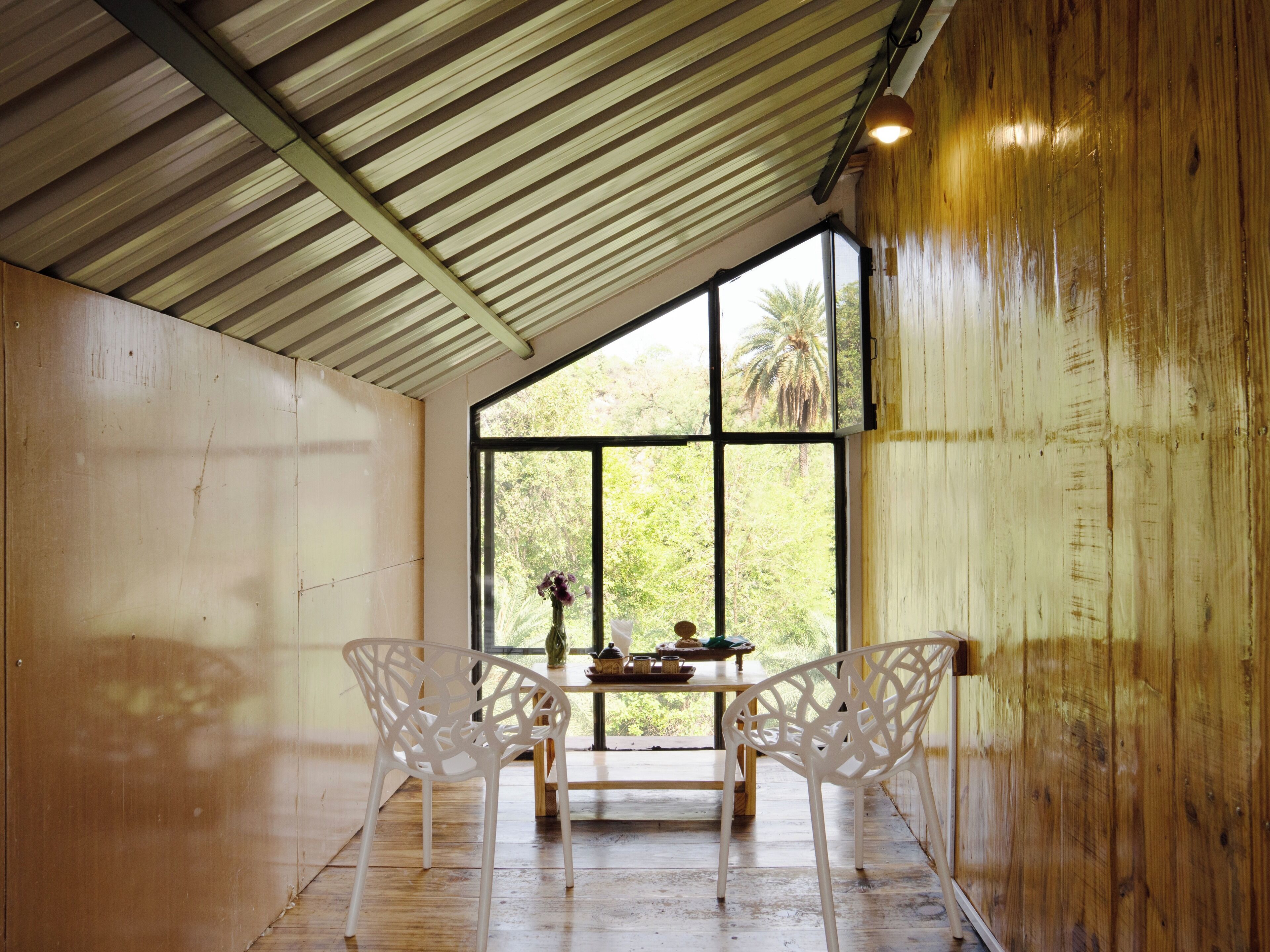 A room with a sloped ceiling, large windows, and two white chairs.