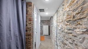 A narrow hallway with stone walls, a white door, and a grey curtain. - Cozy 1BR Near Findlay Market and UC, Rhinegeist (Cincinnati)