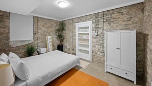 A bedroom with a bed, a wardrobe, a shelf unit, and a stone wall. - Cozy 1BR Near Findlay Market and UC, Rhinegeist (Cincinnati)