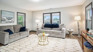 A living room with two sofas, a coffee table, and a lamp. There are windows with blinds and a painting on the wall. - Dunes Getaway! Plush Mattresses! Near Beach! (Michigan City)