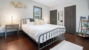 A bedroom with a metal bed frame, a bedside table with a lamp, a mirror, and a wooden floor. - Dunes Getaway! Plush Mattresses! Near Beach! (Michigan City)