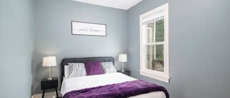 A bedroom with a bed, two bedside tables, a window, and a wall-mounted sign.