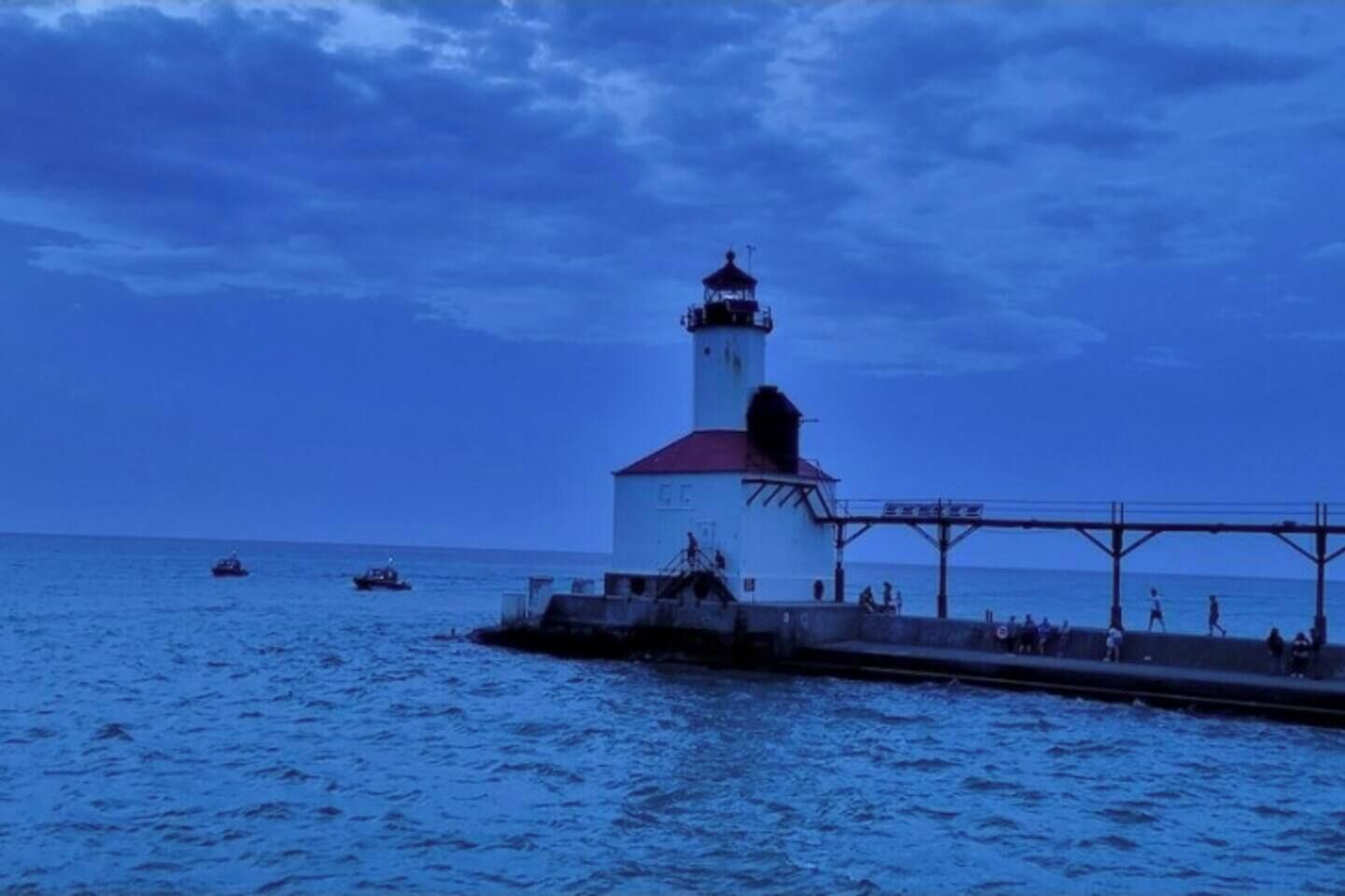Ein Leuchtturm mit rotem Dach und weißem Turm, der auf einem Steg ins Wasser hinausragt.