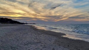 Une plage avec un large rivage sablonneux et des vagues douces, sous un ciel nuageux illuminé par le coucher de soleil.