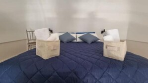 Un lit recouvert d’une courtepointe bleue, deux oreillers et deux tables de chevet avec des boîtes de mouchoirs.