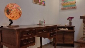 Un bureau en bois avec des tiroirs, un globe terrestre, un petit vase avec une fleur et un meuble en bois dans une pièce dont le sol est recouvert de carreaux.