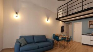 Un salon moderne avec un canapé bleu, une table à manger et des chaises, un escalier et un coin cuisine.