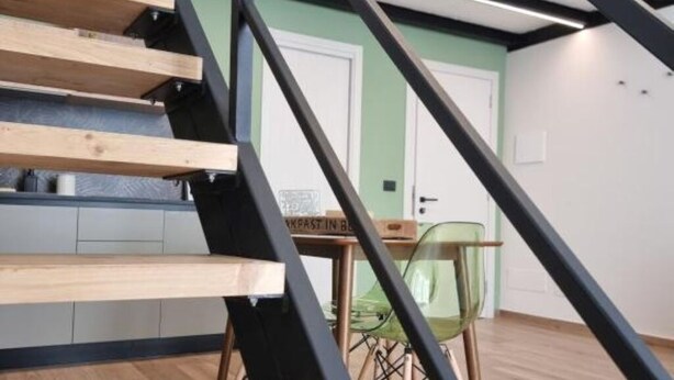 Un escalier avec des marches en bois et des rampes en métal noir, menant à une pièce où se trouvent une chaise verte et une table.