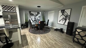 Una cocina moderna con refrigerador empotrado, un comedor con mesa redonda y sillas, y un cuadro abstracto grande en la pared.