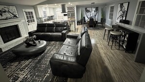 Amplia sala de estar con sofá modular, chimenea y comedor con mesa alta y sillas.