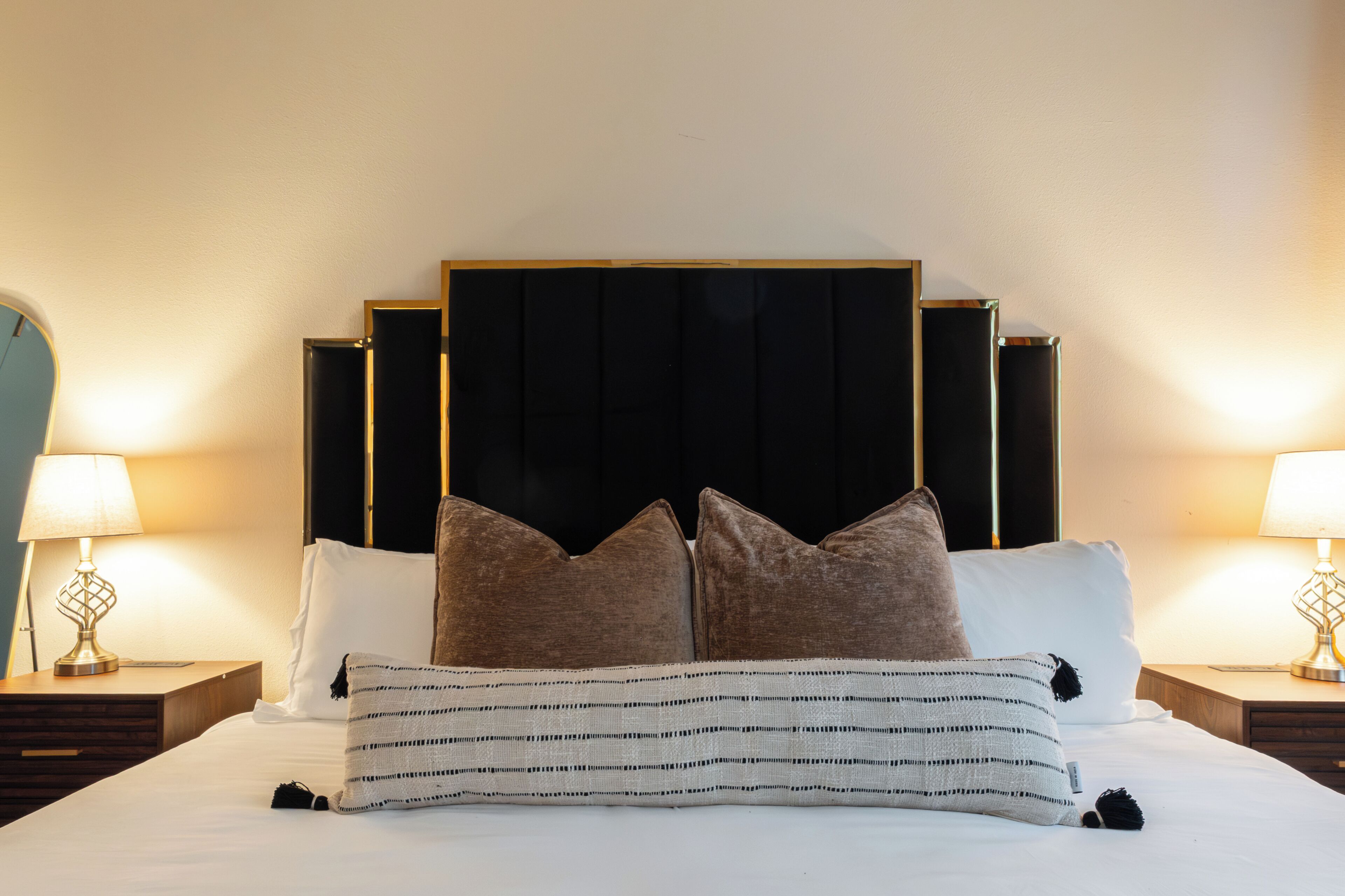 Un lit bien fait, agrémenté d’un coussin rayé et de deux coussins marron, avec deux tables de chevet de chaque côté, sur lesquelles sont posées des lampes.