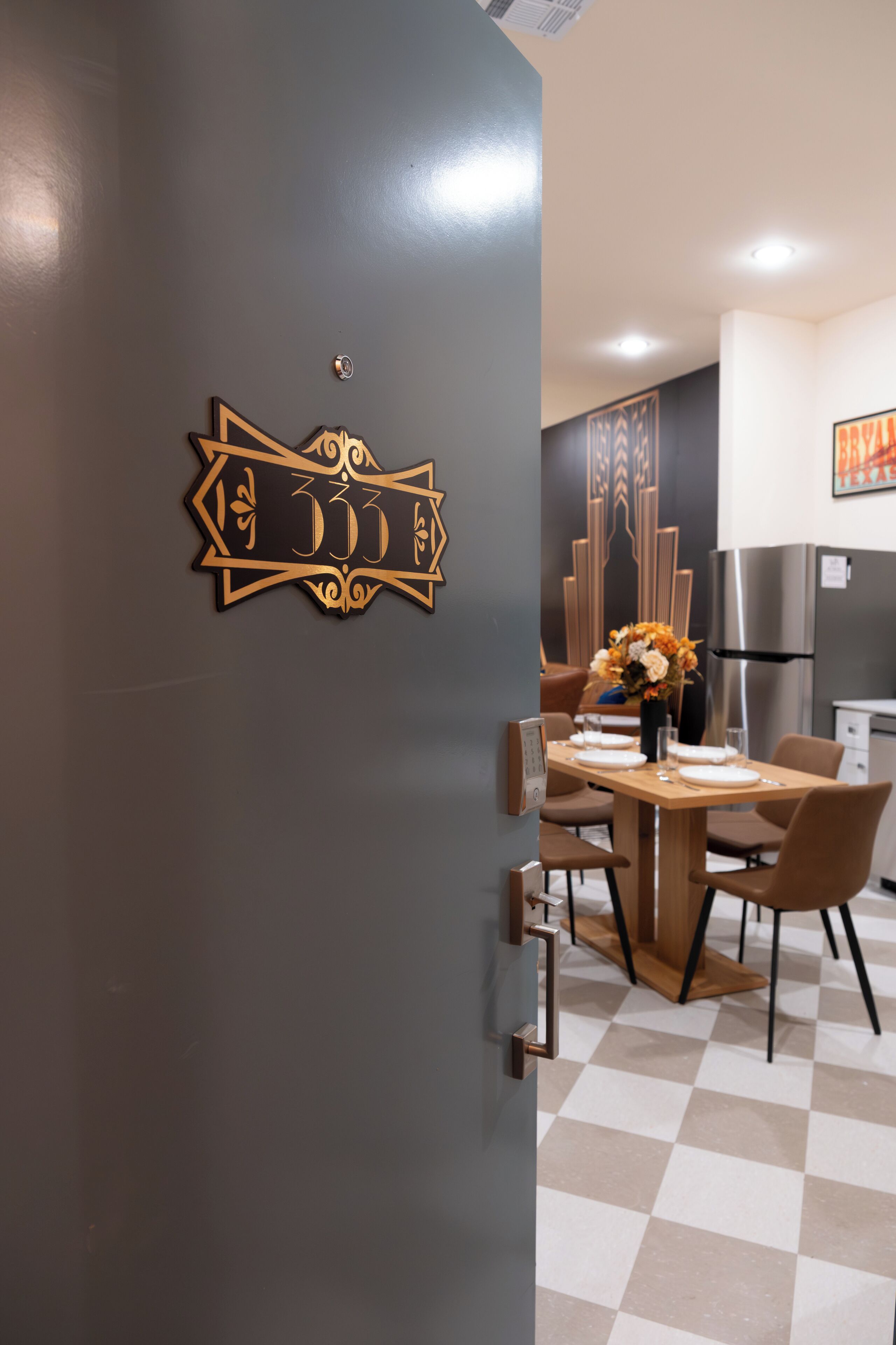 Une cuisine moderne avec un carrelage à motifs, une table à manger en bois avec des chaises et un élément décoratif mural.