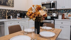 Una cocina moderna con armarios blancos, un microondas de acero inoxidable y una mesa de comedor con platos y vasos.