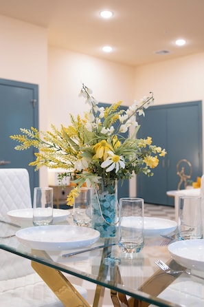 A dining table set with white plates, clear glasses, and a vase with yellow and white flowers.