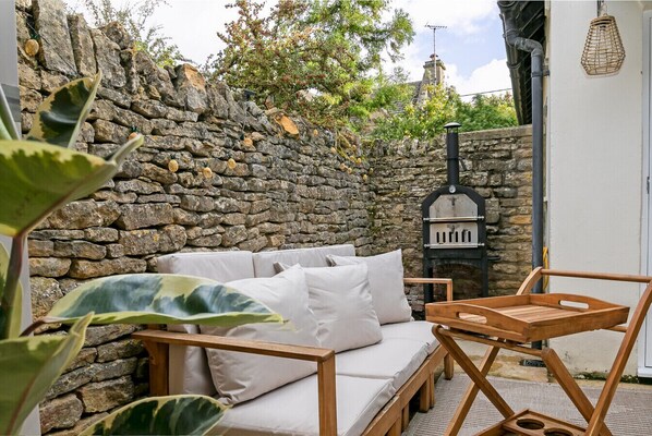 A stone wall, a wooden bench, a white sofa, and a wood-fired oven. - Beautiful 2 Bedroom Cottage in the Cotswolds (churchill)
