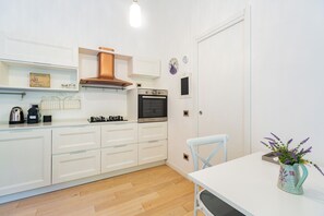 Una cuina moderna amb armaris blancs, una campana extractora d'acer inoxidable, un forn i un petit finestral.