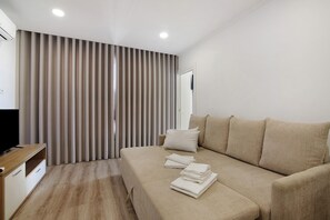 A modern hotel room with a large bed, a TV, and a window with blinds.