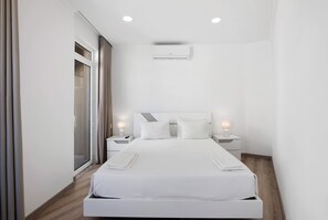 A modern hotel room with a large bed, bedside tables, a ceiling air conditioner, and a sliding glass door.