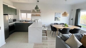 A modern kitchen with a central island, dining area with a round table and chairs, and a large window providing natural light. - Stylish City Retreat - sleeps 6 (Galway)