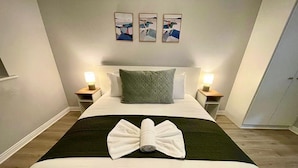 A neatly made bed with a folded towel in the center, two bedside lamps, and three framed pictures on the wall. - Stylish City Retreat - sleeps 6 (Galway)