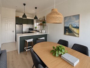 Une cuisine moderne dotée d’un îlot central, de luminaires suspendus et d’un coin repas avec une table et des chaises en bois.