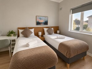 Une chambre d’hôtel avec deux lits, un bureau, une chaise, une fenêtre et un tableau au mur.